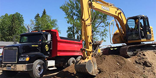 Backhoe digging into dirt near a red dump truck