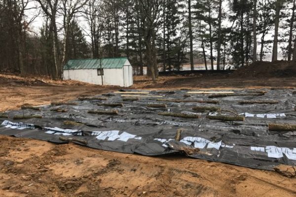 Black tarp held down with logs in front of green roofed building