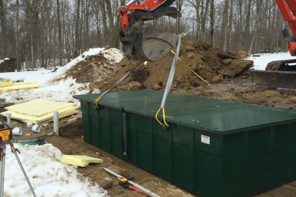 Backhoe lifting large septic tank out of the ground